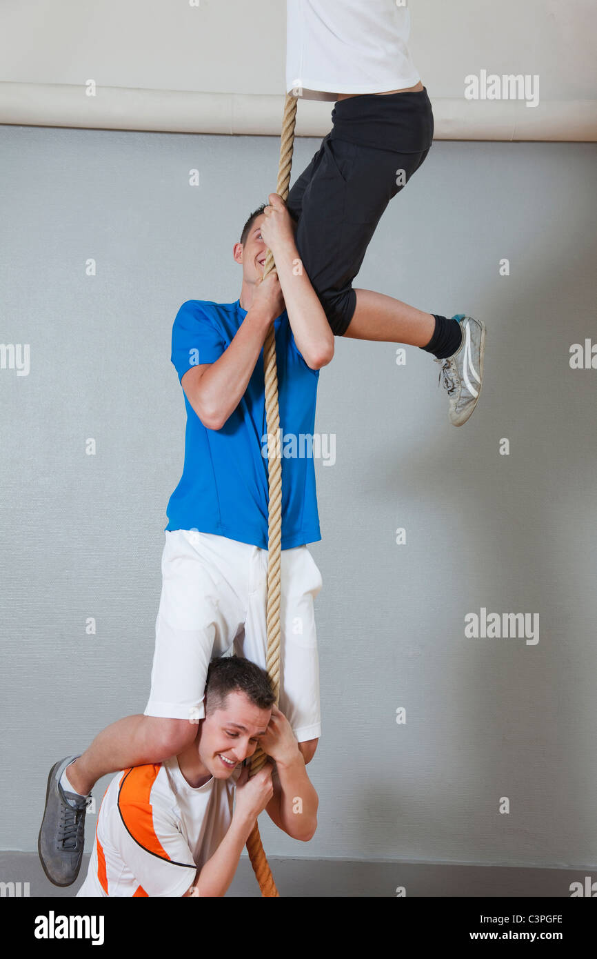 Germania, Berlino, giovani uomini e donne arrampicata corda nella palestra della scuola Foto Stock