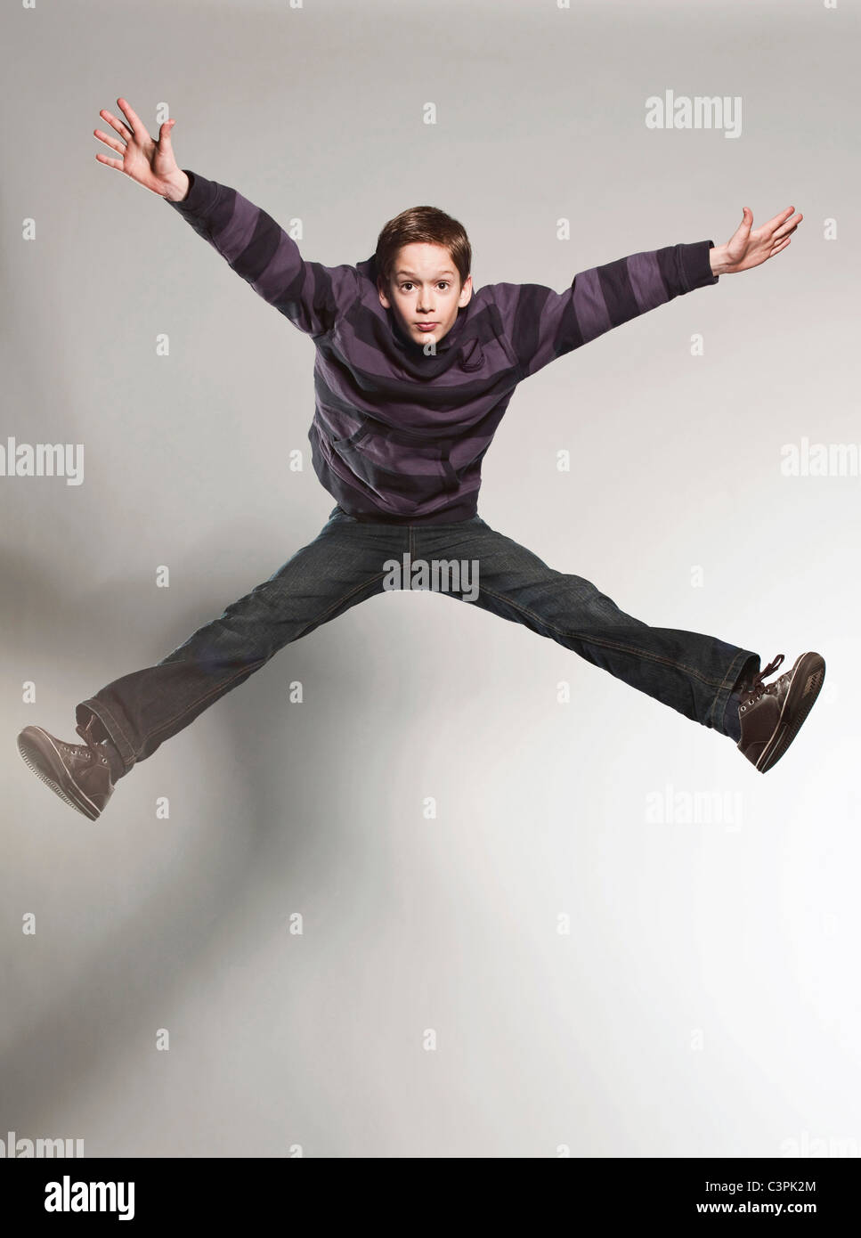 Ragazzo (12-13) jumping contro uno sfondo grigio Foto Stock