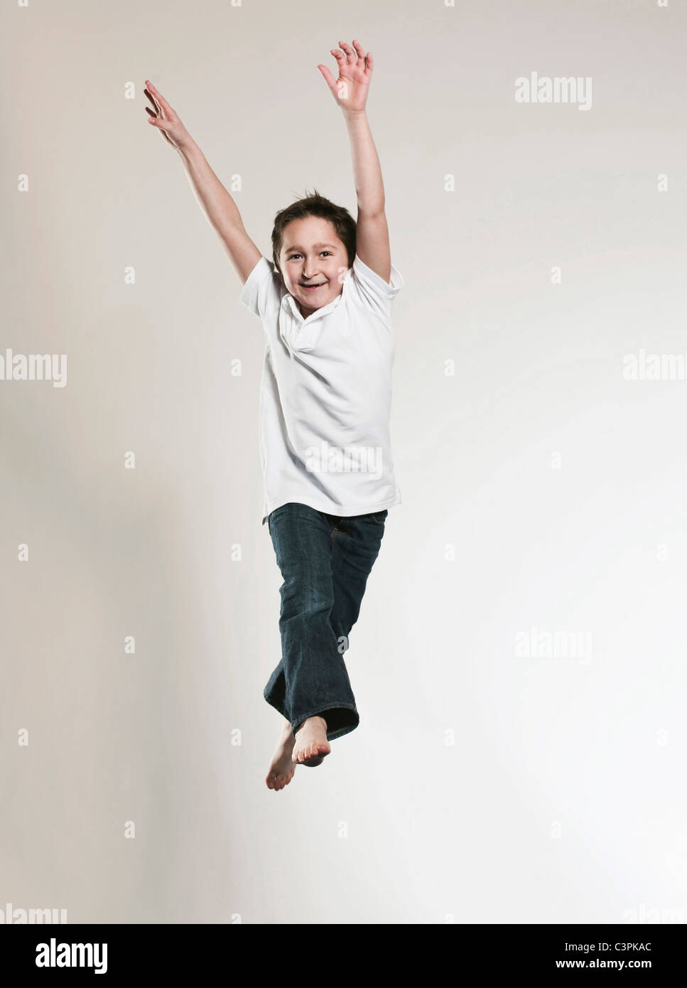 Ragazzo (8-9) salta con le braccia in alto, ritratto, sorridente Foto Stock