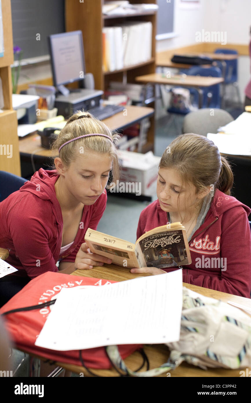 Femmina adolescente Anglo middle school junior alta agli studenti di leggere il libro in brossura insieme al banco in aula Foto Stock