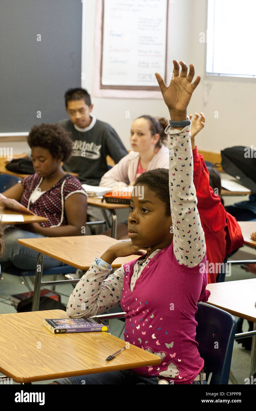 Afro-americano di giovane studentessa alza la mano per rispondere alla domanda nel medio aula scolastica Foto Stock