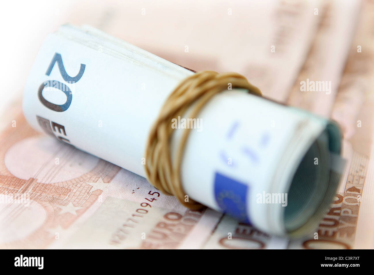 Arrotolato 20 banconote in una fascia elastica sul fuori fuoco 10 le banconote in euro Foto Stock