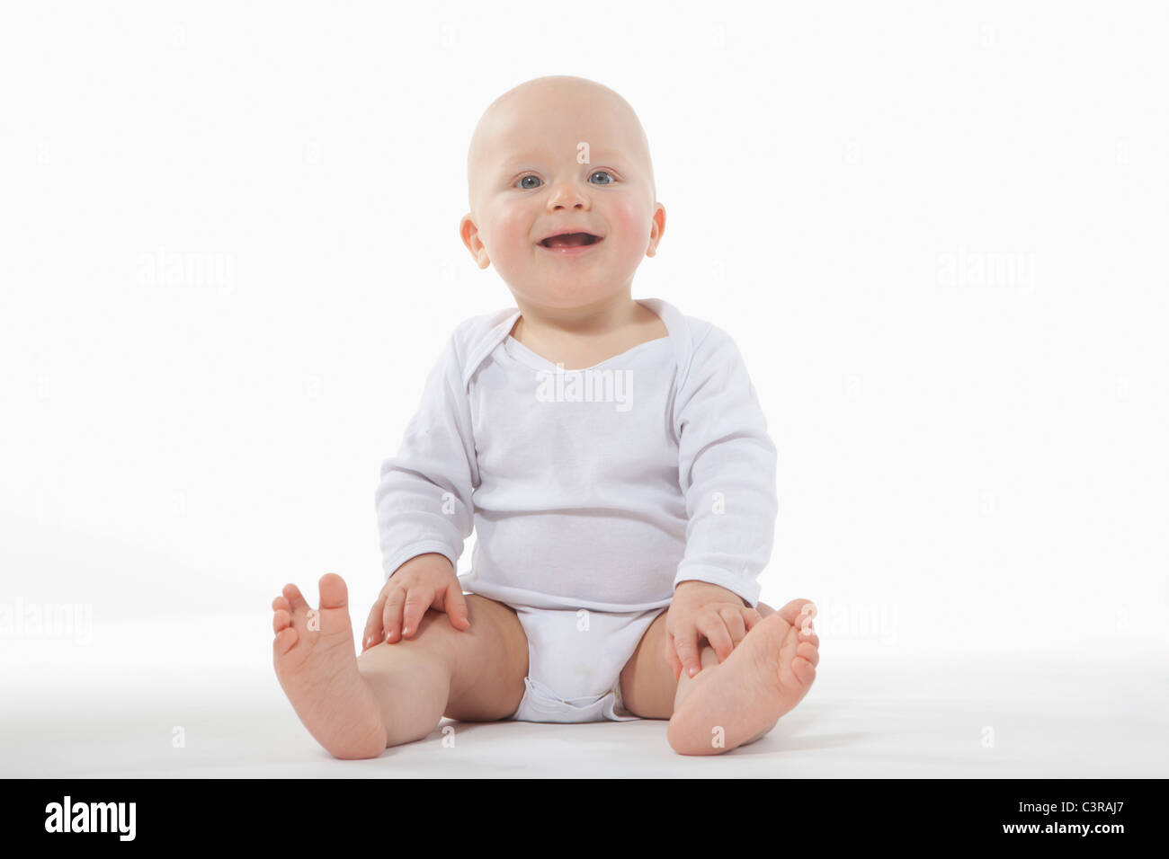 Baby boy (6-11 mesi) seduto sul pavimento, sorridente Foto Stock