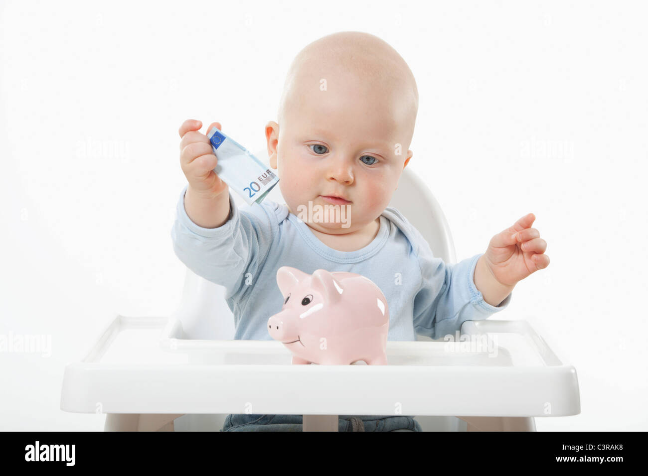 Baby boy (6- 11 mesi) mettendo 20 euro nota nel salvadanaio Foto Stock