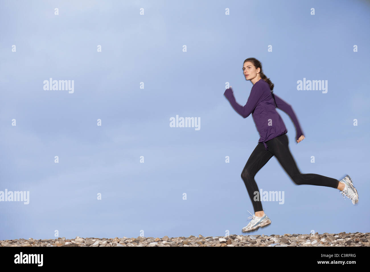 Donna jogging lungo la spiaggia ghiaiosa Foto Stock