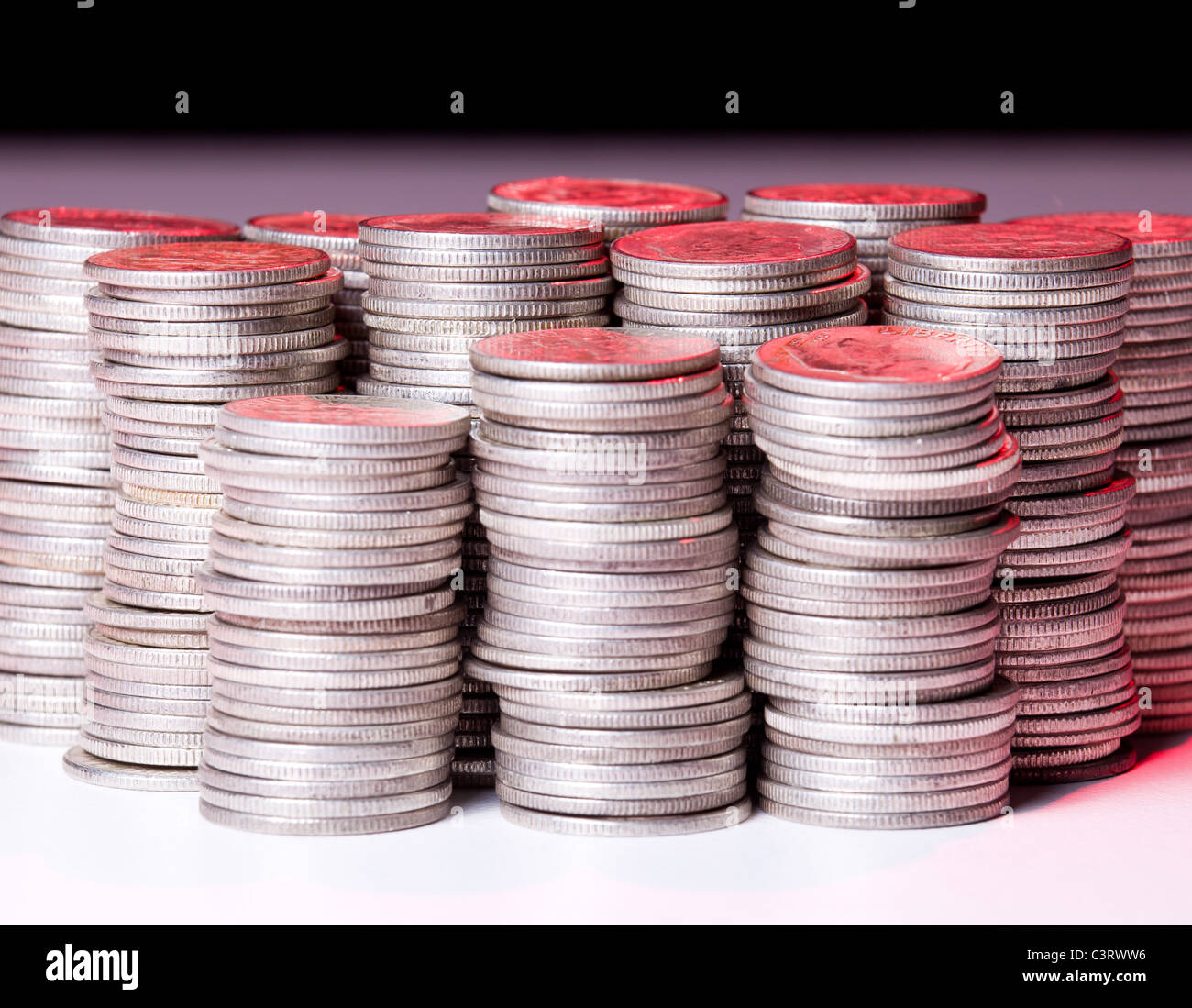 Molte pile di argento vecchio spiccioli di fronte alla telecamera e illuminato con luce rossa Foto Stock