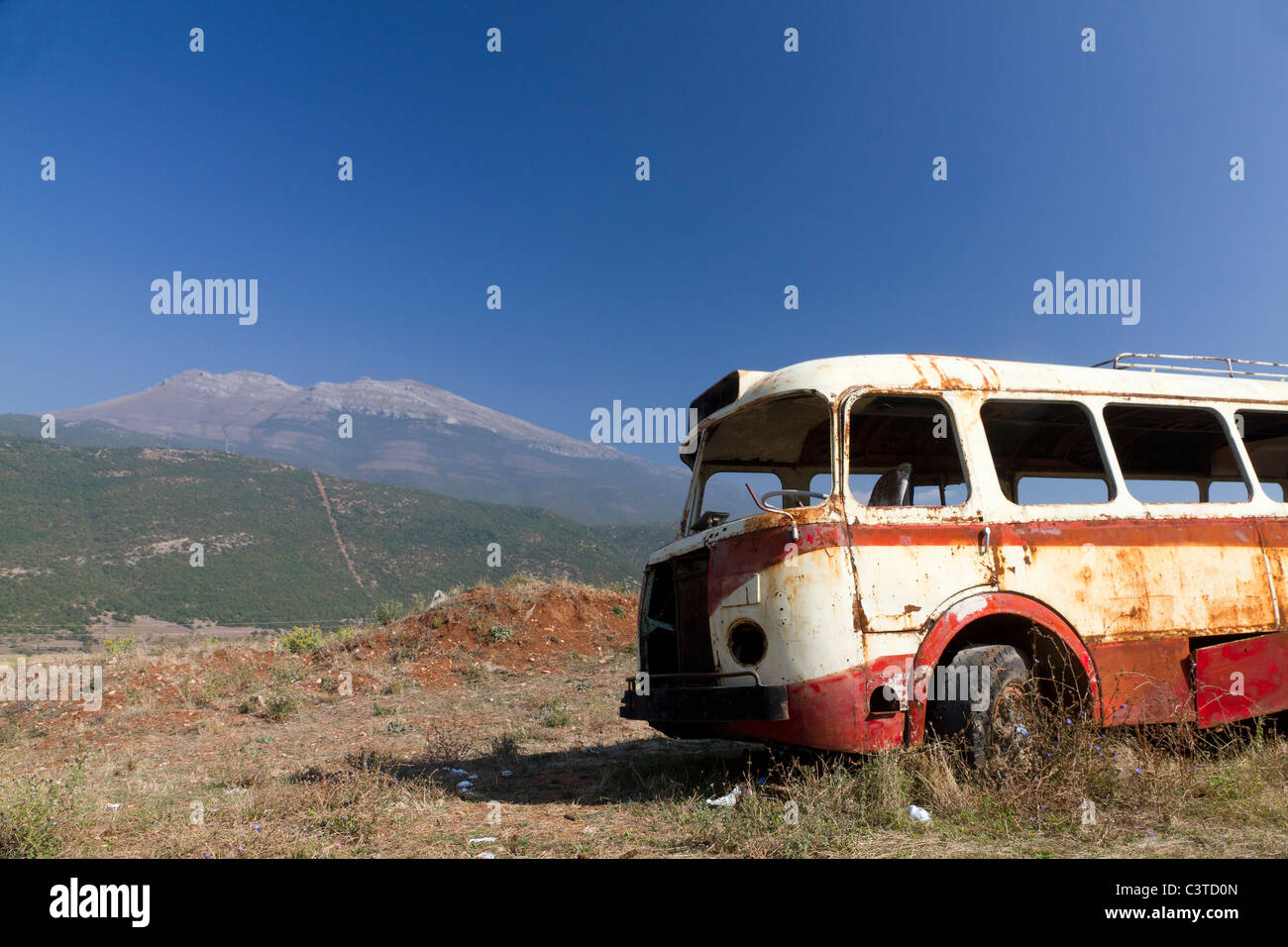 Stripped arrugginito, vecchio abbandonato bus rosso relitto in arido paesaggio montuoso del Montenegro Foto Stock