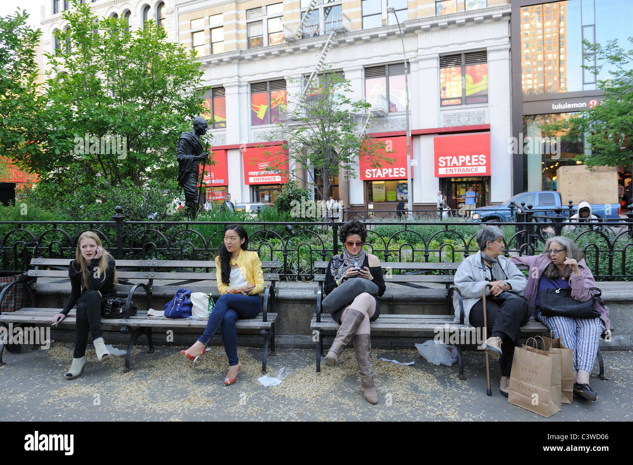 Donna seduta su una panchina in Manhattan's Union Square Park, con una statua di Gandhi in background. Foto Stock