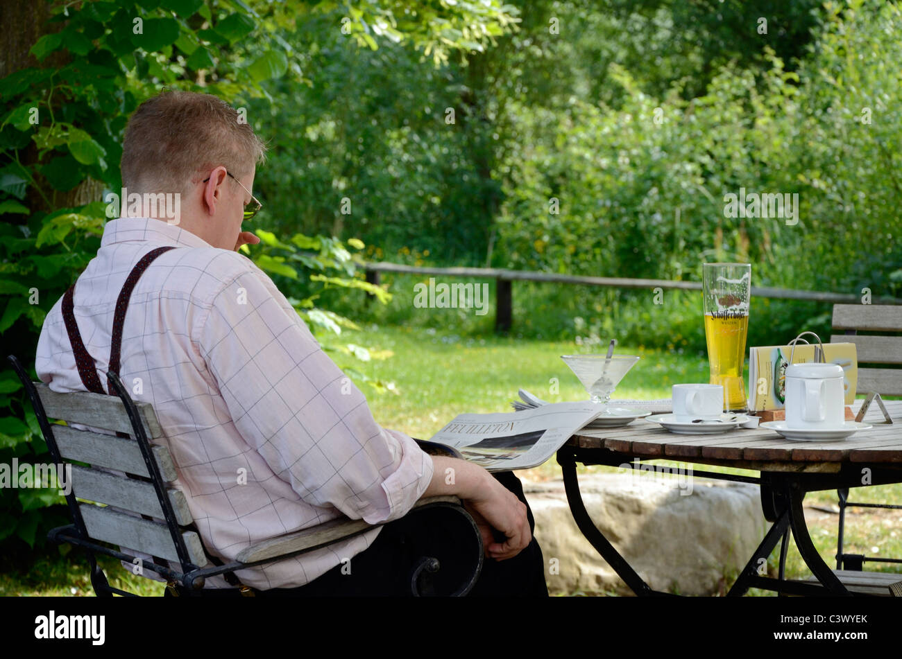 Beer garden cafe rilassante pinta di birra in vetro di frumento gelato caffè quotidiano di lettura di pagine di arti feuilleton uomo lettore di occhiali da bere Foto Stock