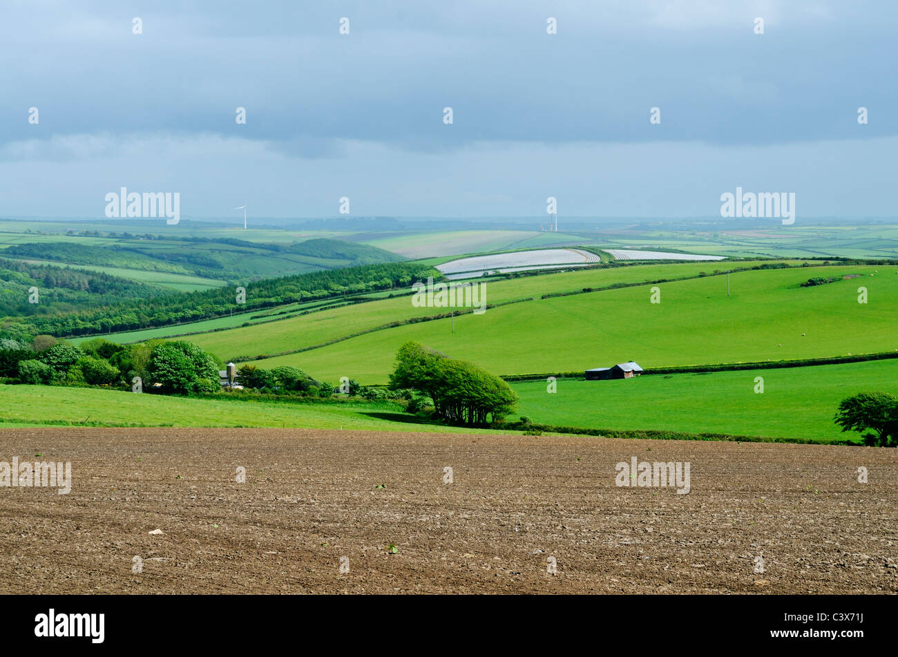 Un campo arato e le colline ondulate del Devon del Nord con nuove turbine eoliche che sono erette in lontananza. Woolacombe, Devon, Inghilterra. Foto Stock