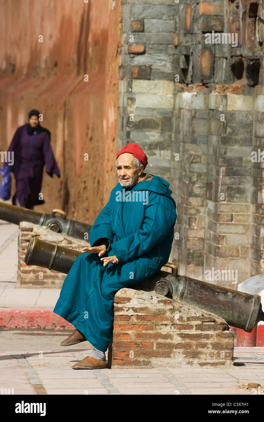 Uomo anziano in abito tradizionale di appoggio e soliloquizing su un cannone a Bab Agnaou, uno di Marrakech il grande gateway, Marocco Foto Stock