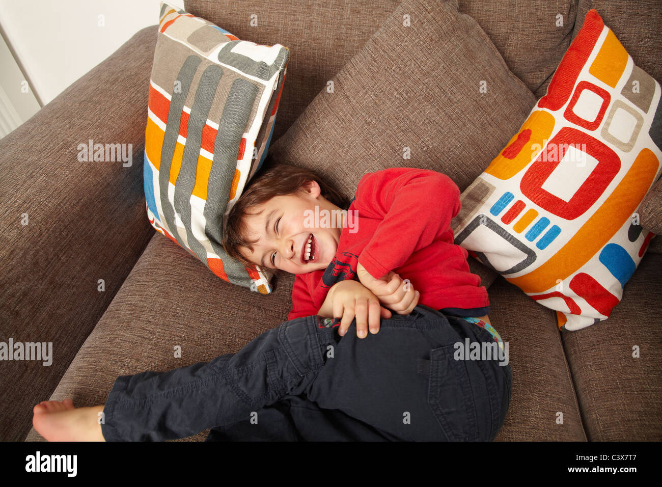 Ragazzo giovane ridere sul divano Foto Stock