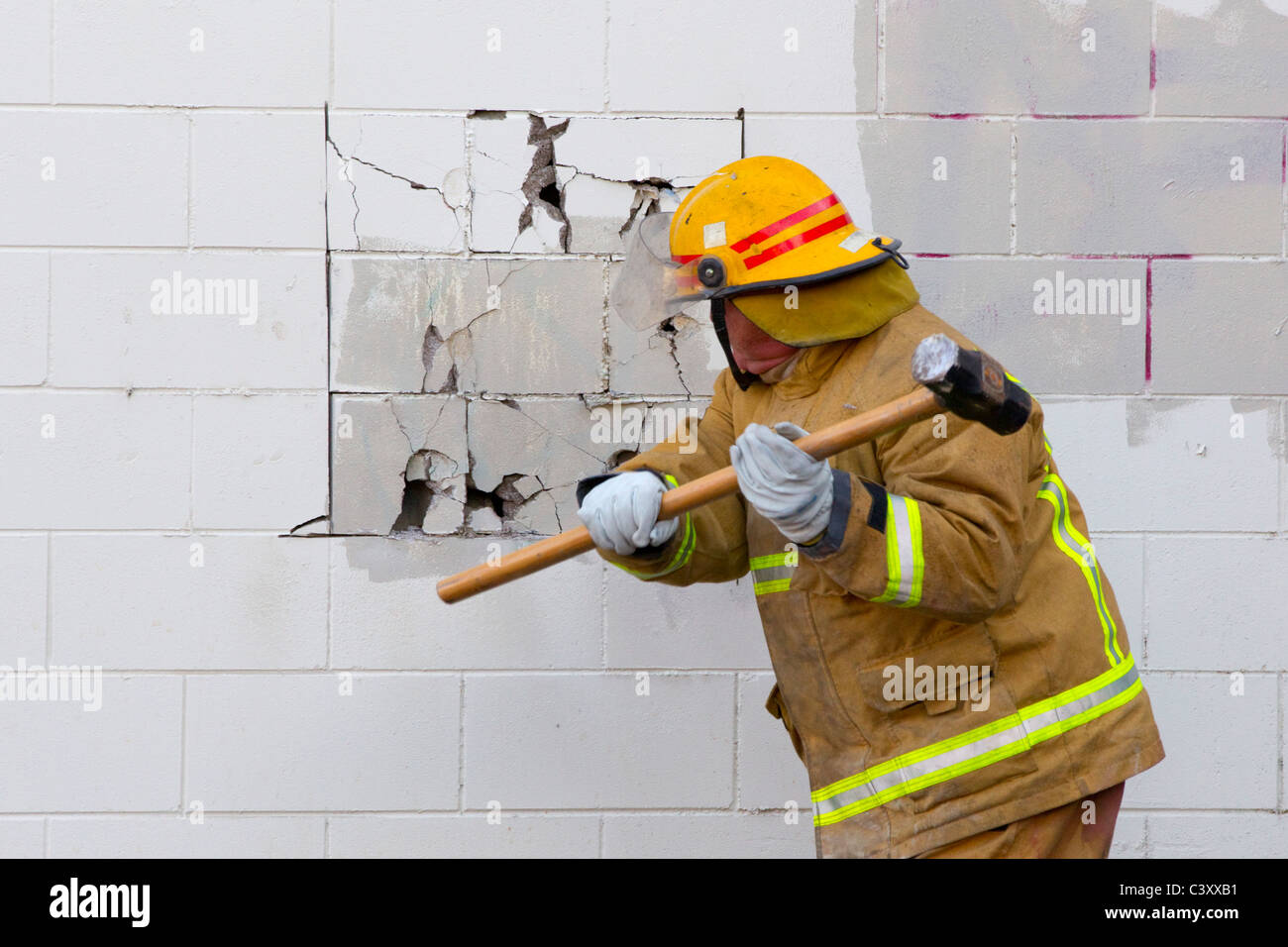Un vigile del fuoco si rompe un muro per accedere a un incendio in una fabbrica, Elliott Street, Auckland Foto Stock
