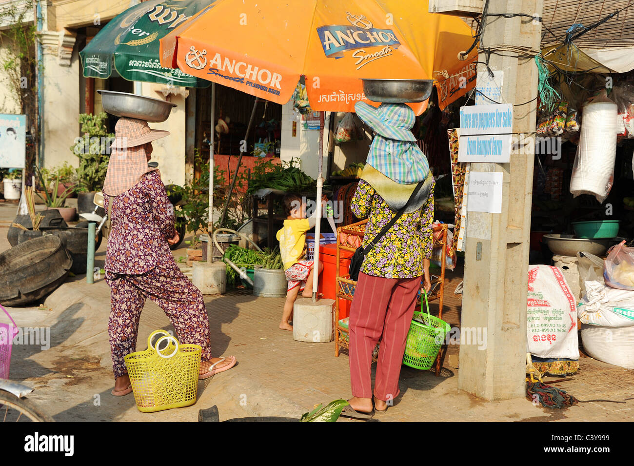 Due Cambogia donna con grandi contenitori sulle loro teste in attesa al di fuori di un negozio a Kampot, Cambogia. Foto Stock