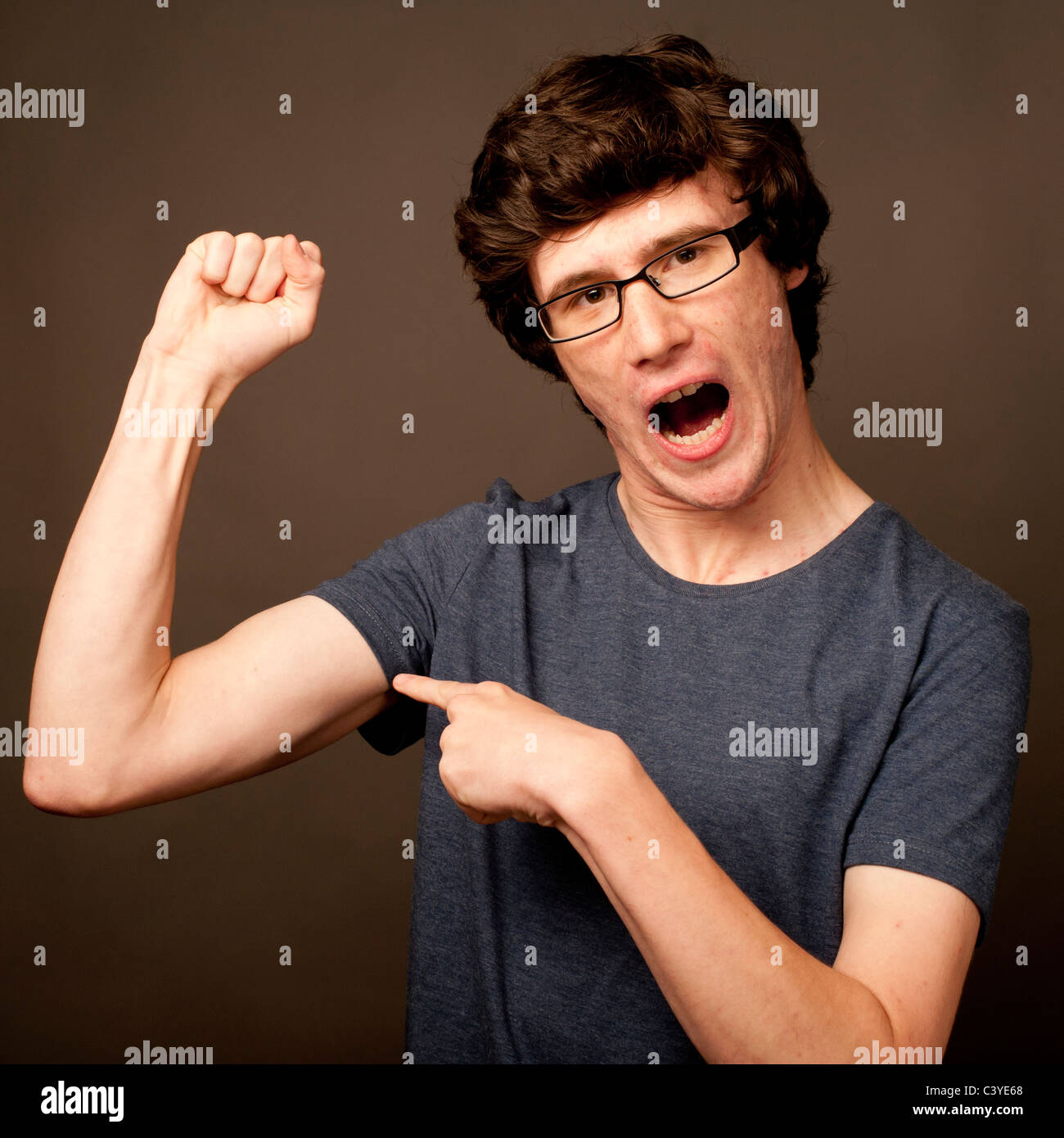 Una debole debole geek nerd giovane con sottili bracci che indossano occhiali flettendo i suoi muscoli Foto Stock