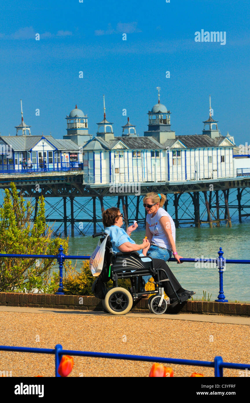 Donna anziana in una sedia a rotelle in chat con una giovane donna sul lungomare di Eastbourne, East Sussex, Regno Unito Foto Stock