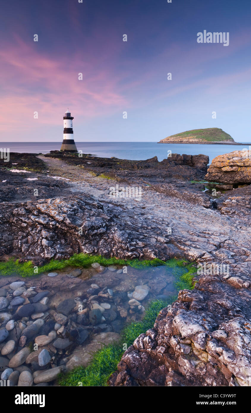 Twilight sulla rocciosa costa di Anglesey guardando verso Penmon Point Lighthouse e isola dei puffini, Anglesey, Galles del Nord Foto Stock