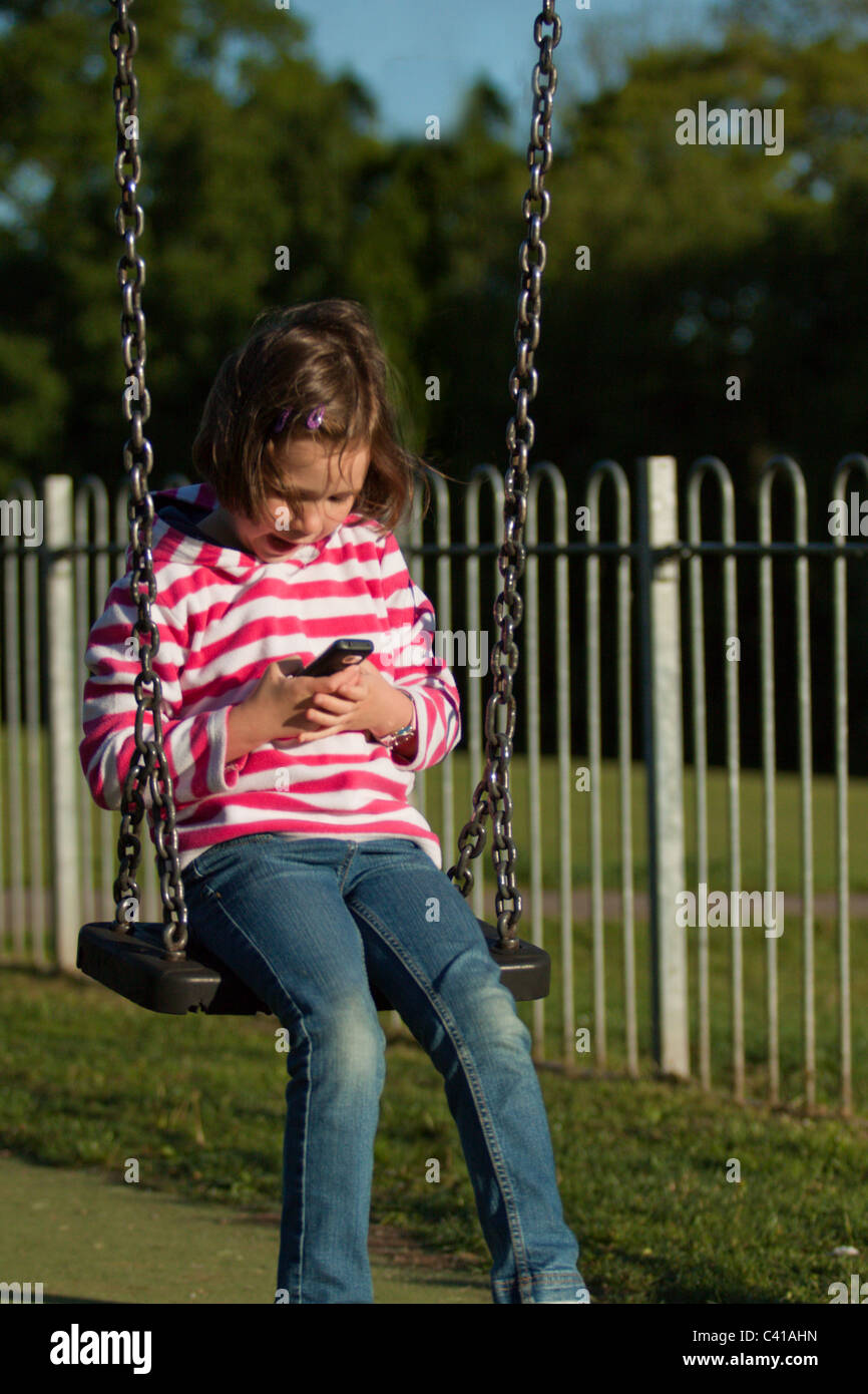 Ragazza giovane con un telefono cellulare presso il parco locale Foto Stock