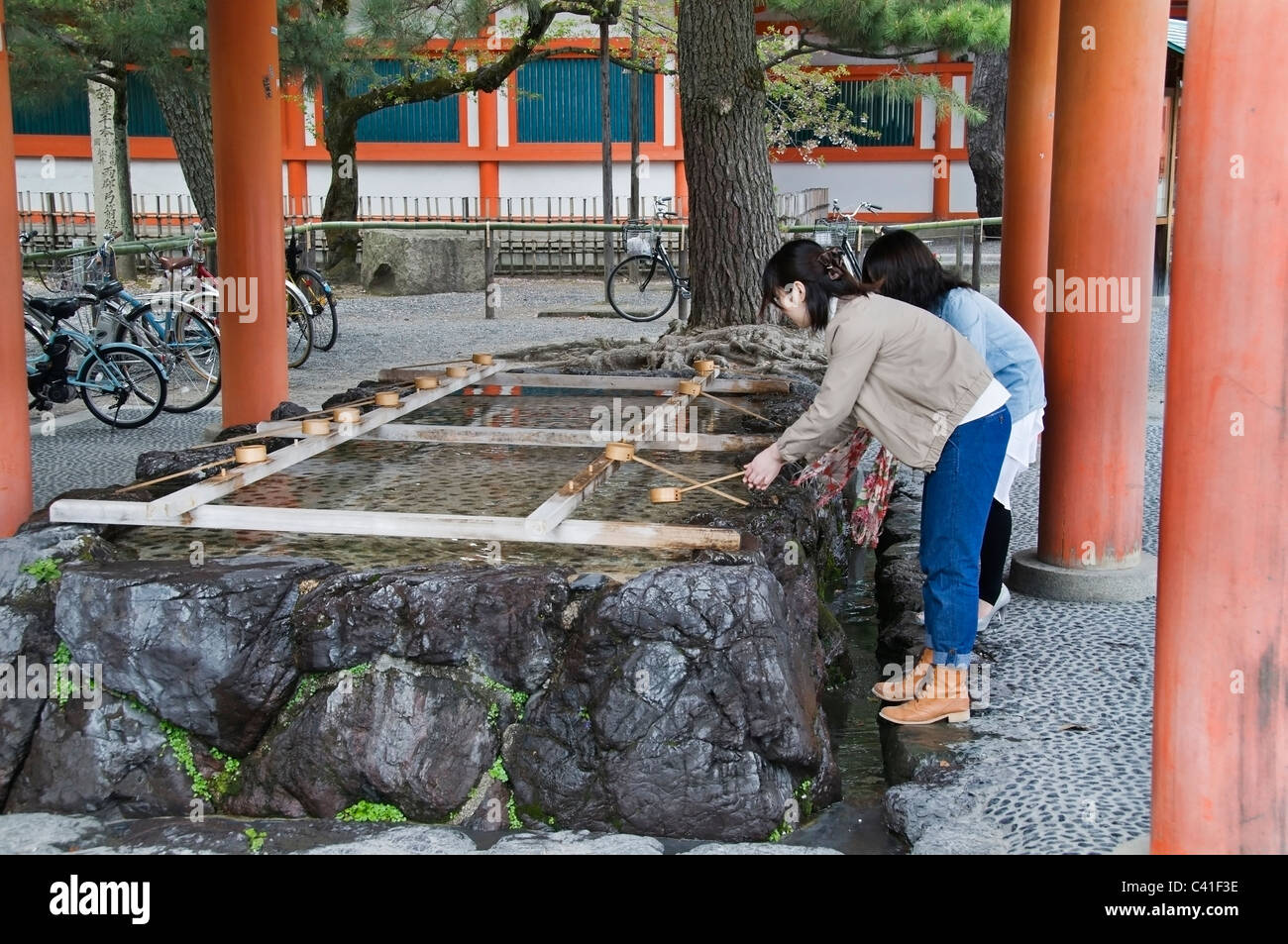Due giovani donne pratica Temizu, un cerimoniale rituale di pulizia ad un lavaggio a mano e purificazione fontana al Santuario Heian-Jingu Foto Stock