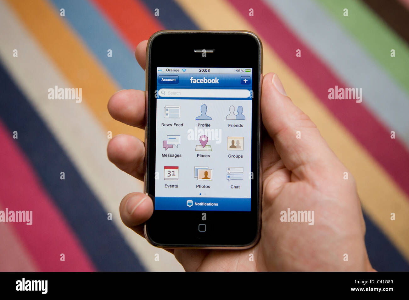 Stretta di mano di sesso maschile in possesso di un iPhone per scegliere dal suo menu Facebook. (Solo uso editoriale). Foto Stock
