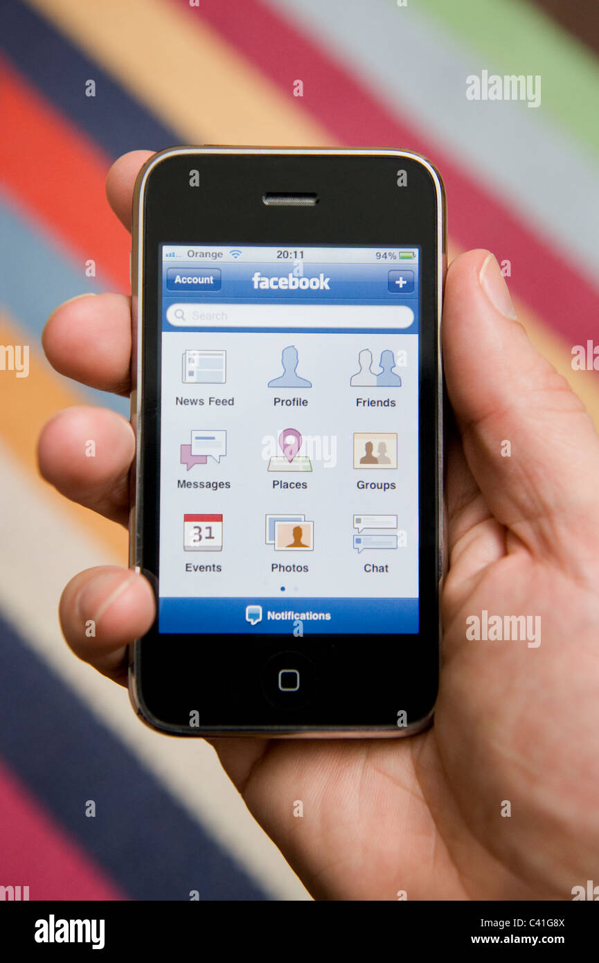 Stretta di mano di sesso maschile in possesso di un iPhone per scegliere dal suo menu Facebook. (Solo uso editoriale). Foto Stock