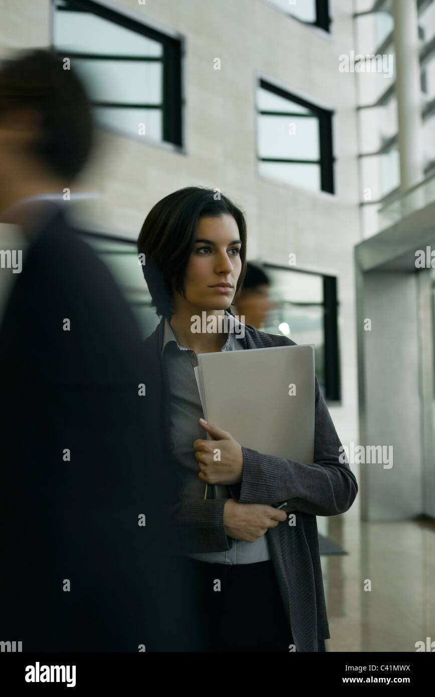 Professional donna in piedi nella lobby che guarda lontano nel pensiero come dirigenti a piedi passato Foto Stock