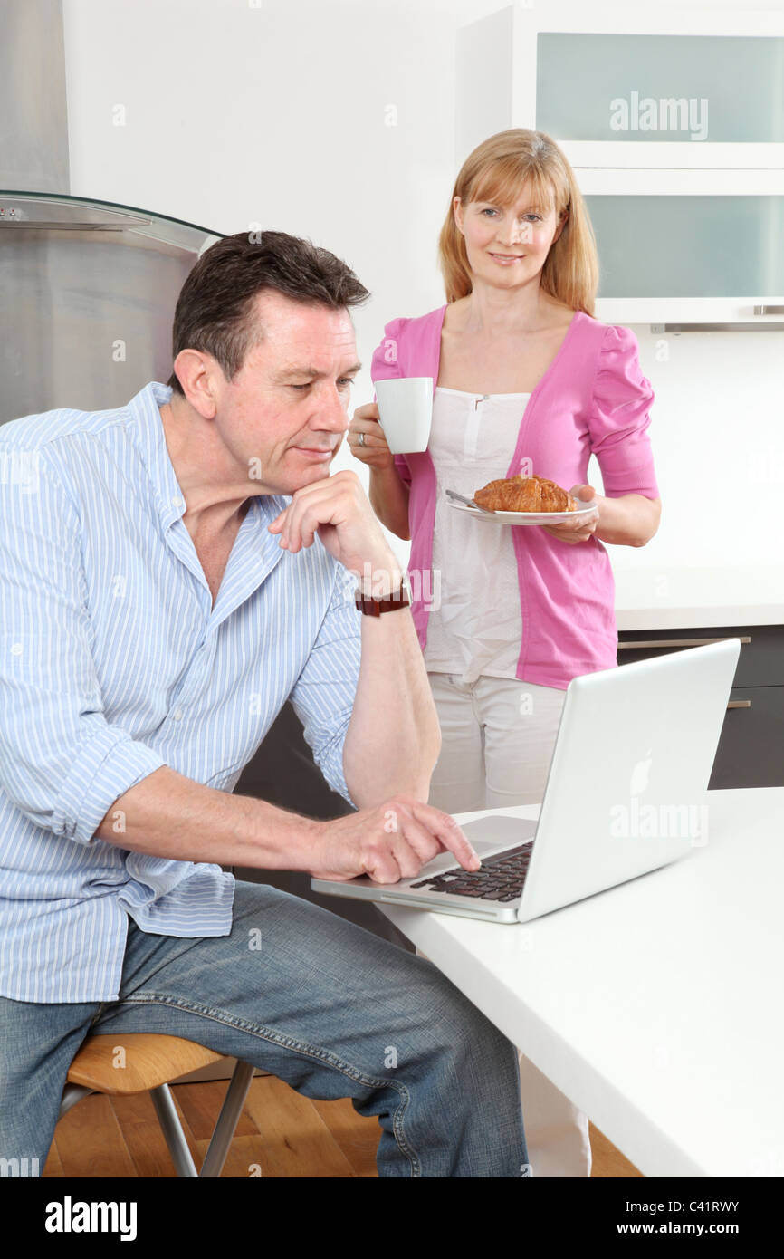Uomo seduto usando un portatile a casa, la donna tenendo una tazza di tè.Accessori per caffè guardando a. Foto Stock