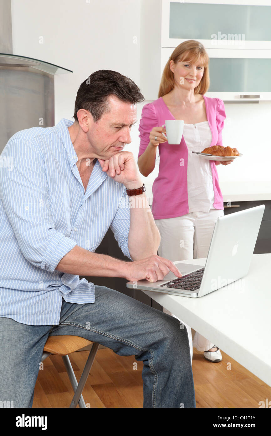 Uomo seduto usando un portatile a casa, la donna tenendo una tazza di tè.Accessori per caffè guardando a. Foto Stock