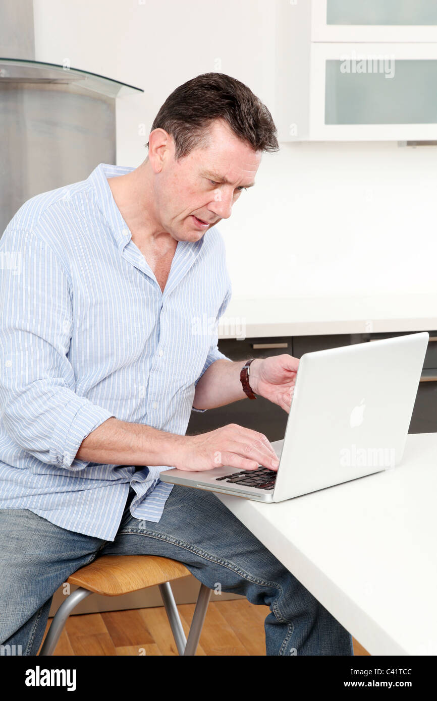 Uomo di casa utilizzando il suo laptop in cucina. Foto Stock