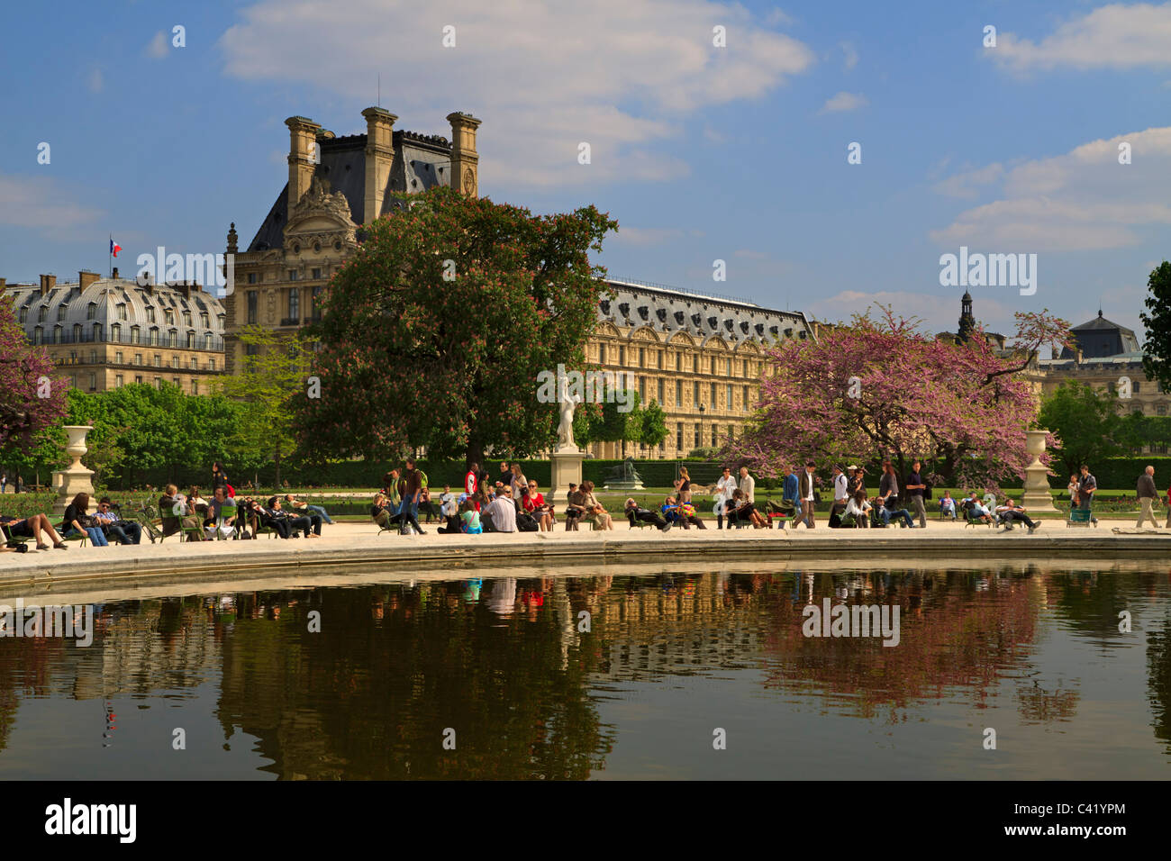 Turisti e parigini rilassatevi nel sole di primavera intorno ad una delle piscine fontana nei Jardins de Tuileries Foto Stock
