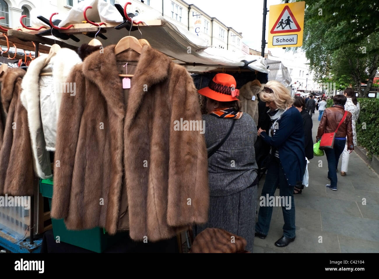 Una donna che acquista e commerciante di mercato su una pelliccia d'epoca  Giacca da cappotto in vendita su un abbigliamento antico Portobello Road  Vecchio mercato di pellicce stallo a Notting Hill West