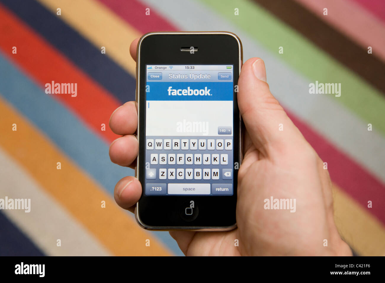 Stretta di mano di sesso maschile in possesso di un iPhone in procinto di aggiornare il proprio stato di Facebook. (Solo uso editoriale). Foto Stock