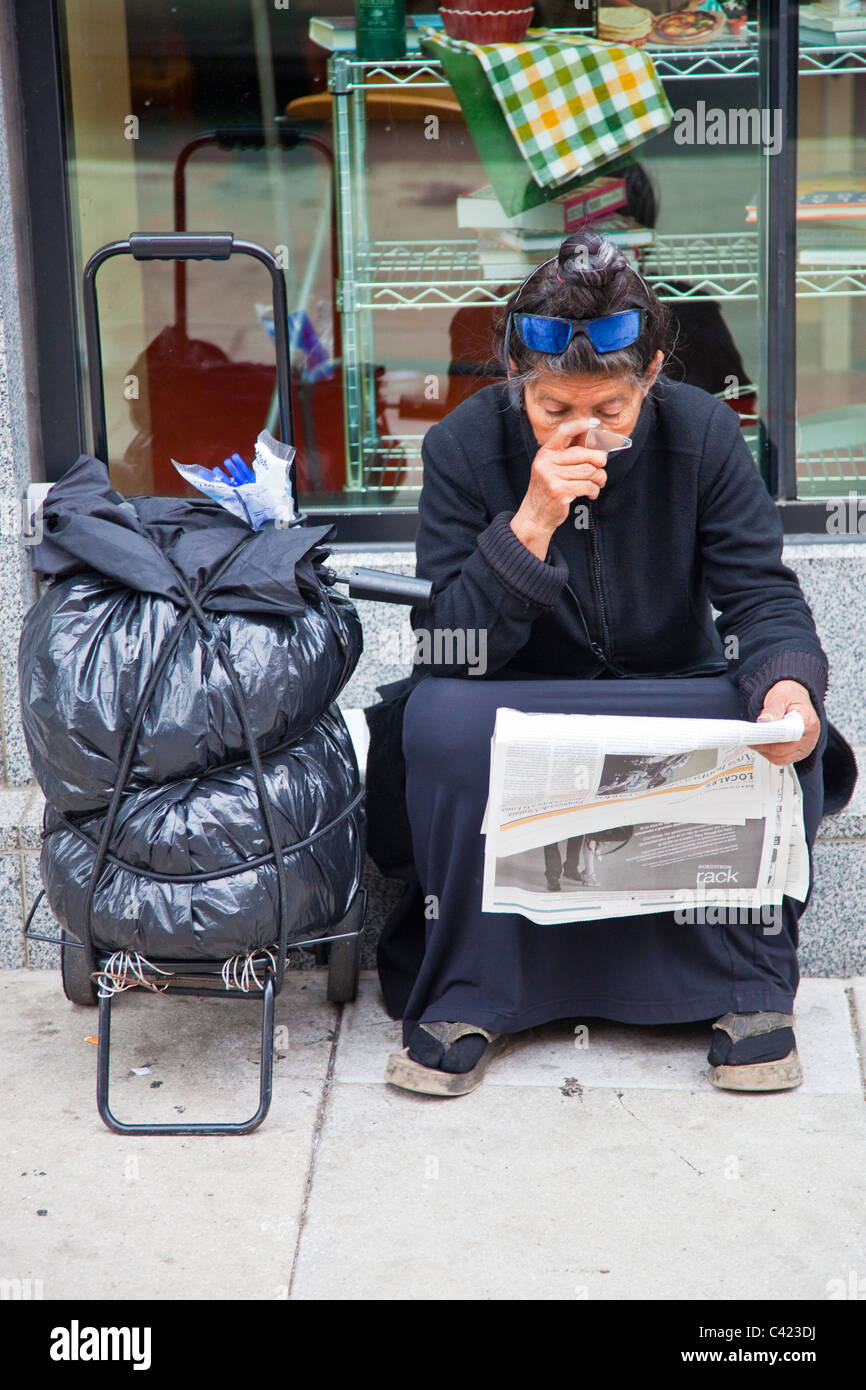 Donna senzatetto utilizzando un fondo di una bottiglia rotta per leggere il giornale, Washington DC Foto Stock