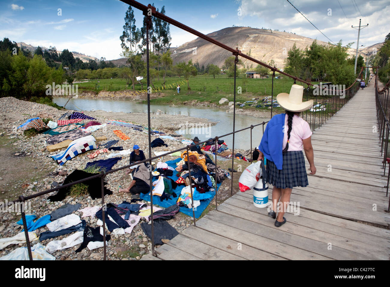 Il Perù, Otuzco, donna indiana con il tipico hat attraversando ponte di sospensione. Background: persone a lavare i panni nel fiume. Foto Stock