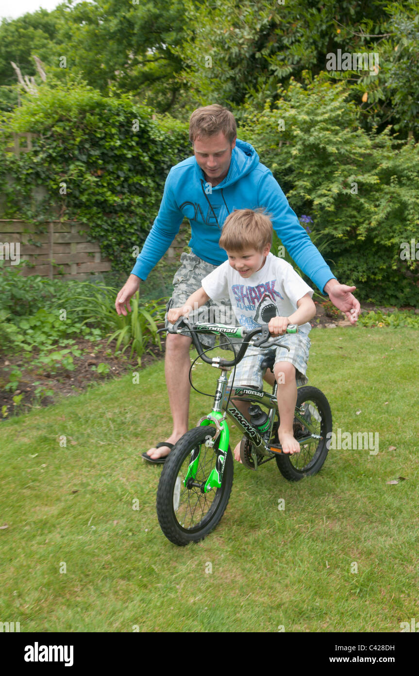 Padre nel giardino sul retro insegnando il suo figlio ad andare in bicicletta Foto Stock
