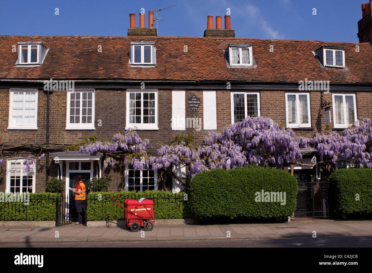 Una donna post con un carrello di consegna Consegna post a Peg Woffington in casa Teddington High Street sulla soleggiata mattina di primavera Foto Stock