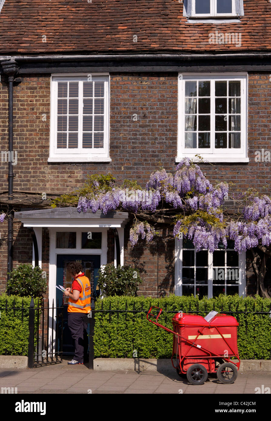 Una donna post con un carrello di consegna Consegna post a Peg Woffington in casa Teddington High Street sulla soleggiata mattina di primavera Foto Stock