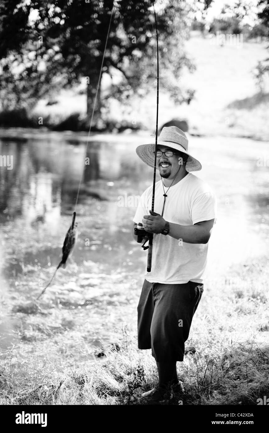 Uomo asiatico la pesca sul lago di cattura del pesce mentre indossa un cappello bianco e nero Foto Stock