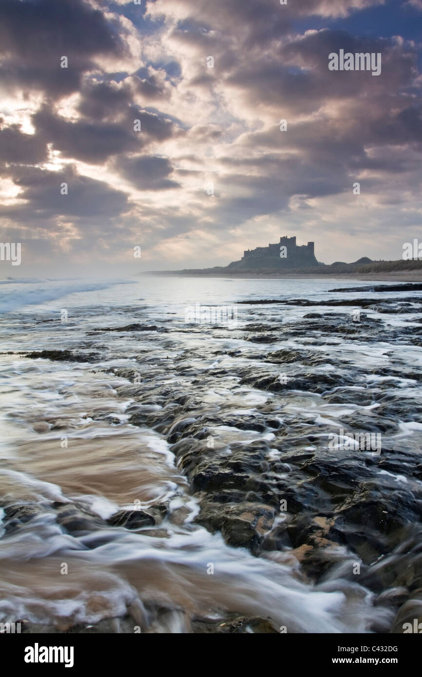 Il castello di Bamburgh alla prima luce da una pedana Whin ripiano di roccia a nord del castello, Northumberland, Inghilterra Foto Stock