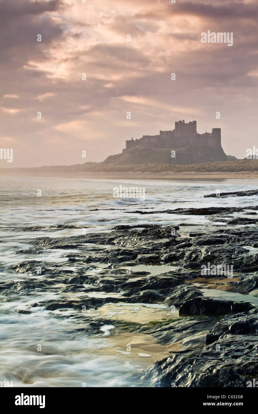 Il castello di Bamburgh alla prima luce da una pedana Whin ripiano di roccia a nord del castello, Northumberland, Inghilterra Foto Stock