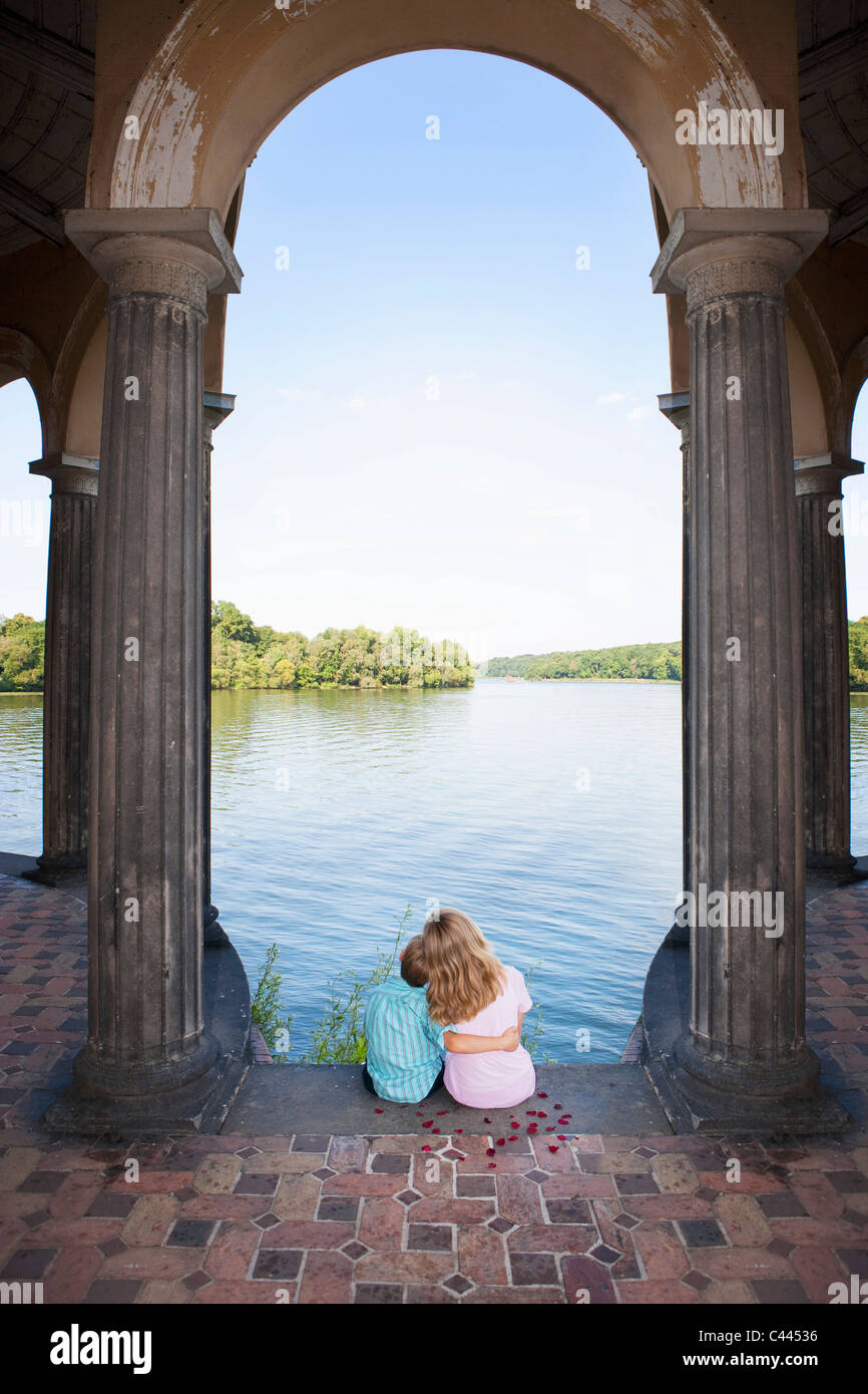 Due bambini seduti insieme sotto un arco accanto a un lago Foto Stock