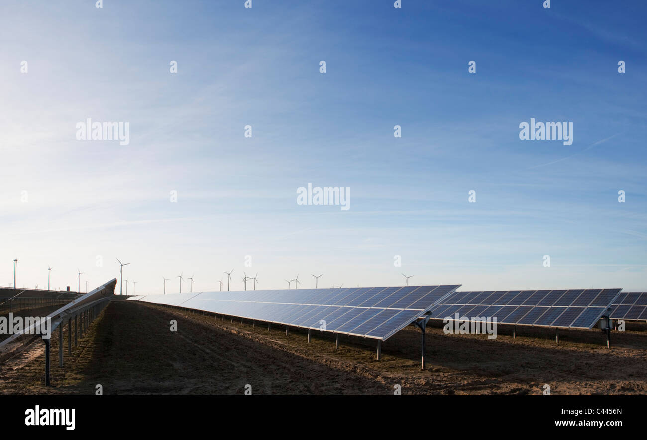 Pannelli solari in un campo e delle turbine a vento a distanza Foto Stock
