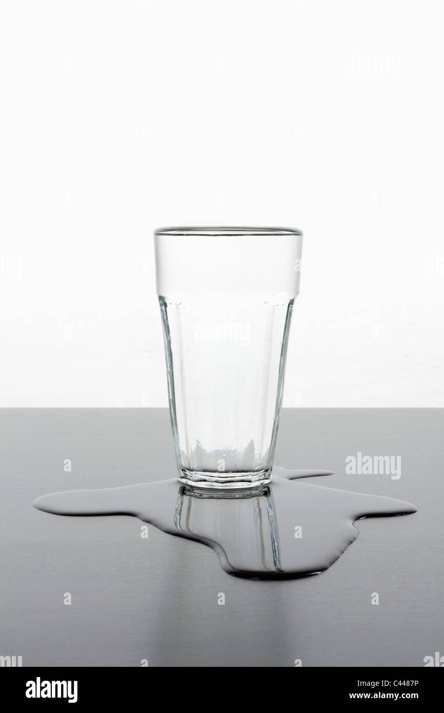 Un montante del vetro in piedi in una pozza d'acqua versata Foto Stock