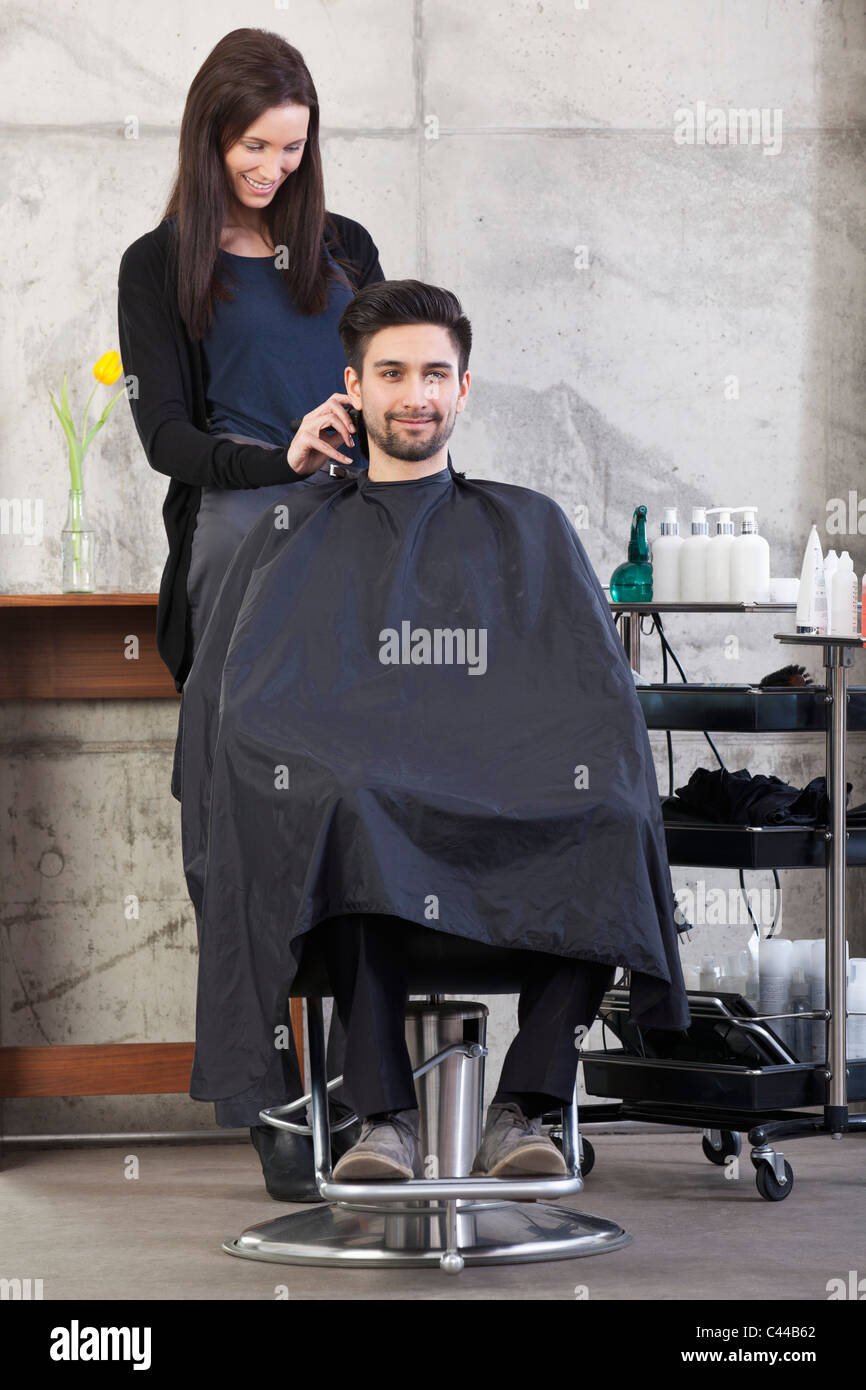 Un parrucchiere utilizzando clippers su un cliente maschio Foto Stock