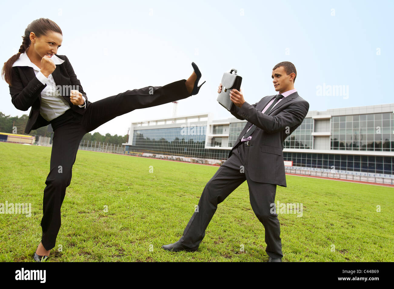 Ritratto di imprenditore proteggere se stesso con valigetta mentre aggressivo imprenditrice facendo kick da gamba Foto Stock