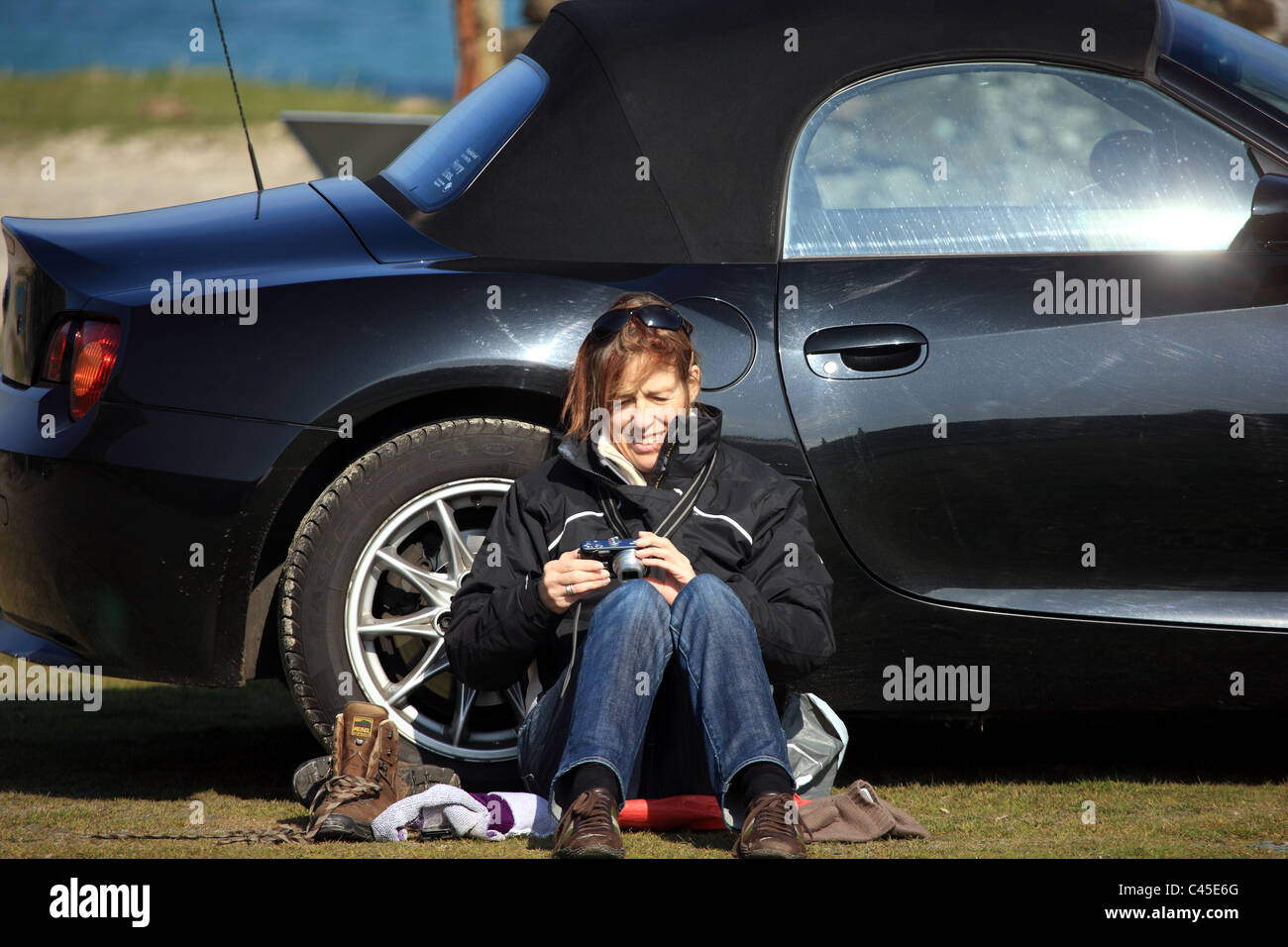 Donna appoggiata contro la sua auto guardando le foto sul suo fotocamera dopo una passeggiata Foto Stock