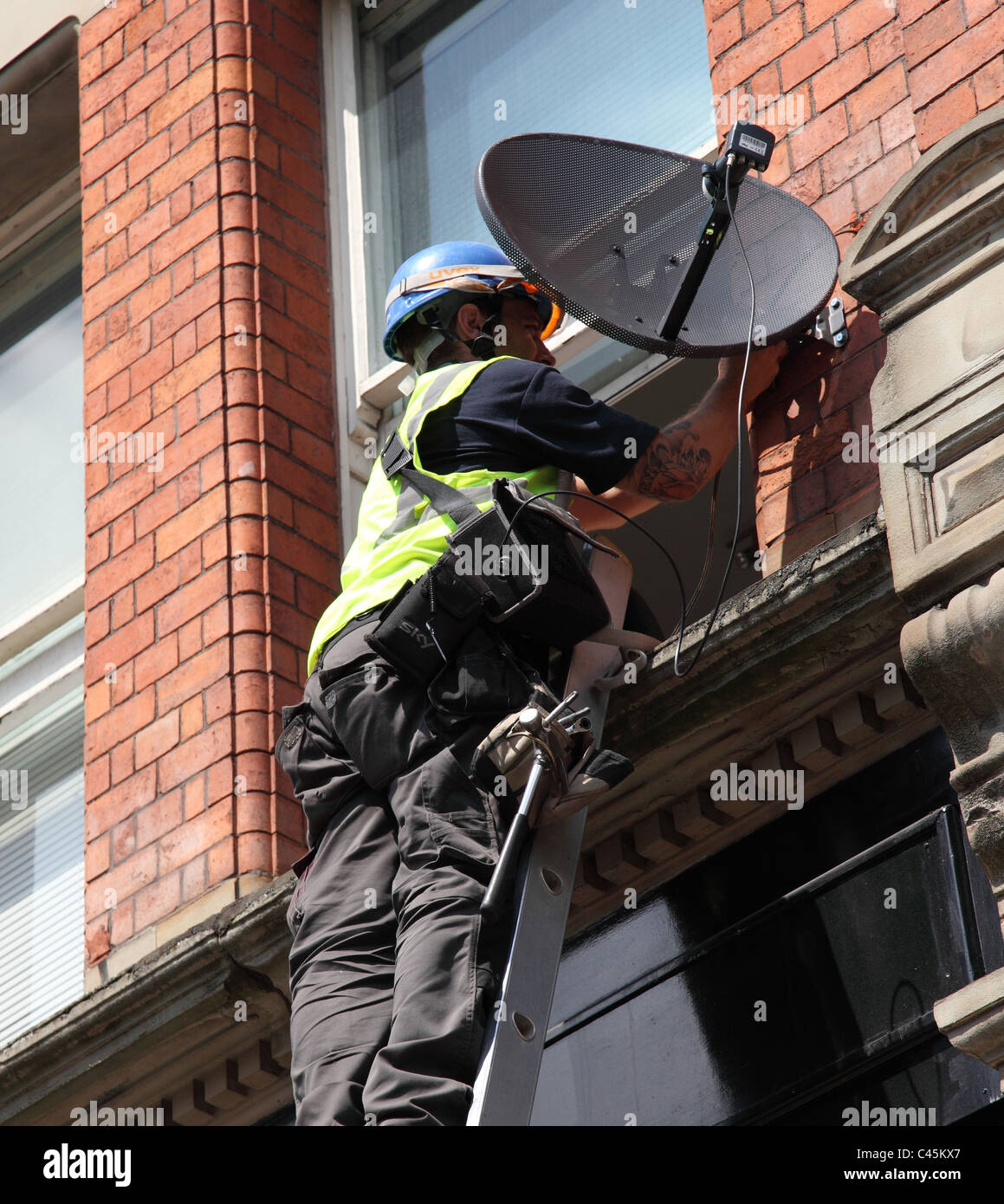 Un ingegnere di installare una parabola satellitare ad un edificio in U.K. Foto Stock