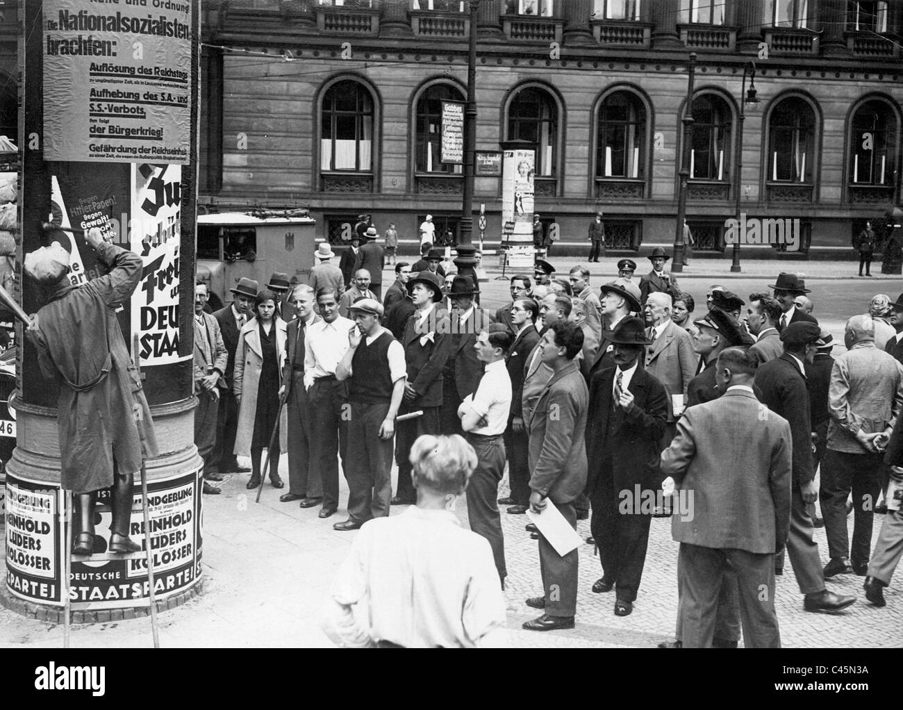 Pedoni nella parte anteriore del pilastro della pubblicità con pubblicità elettorale, 1932 Foto Stock