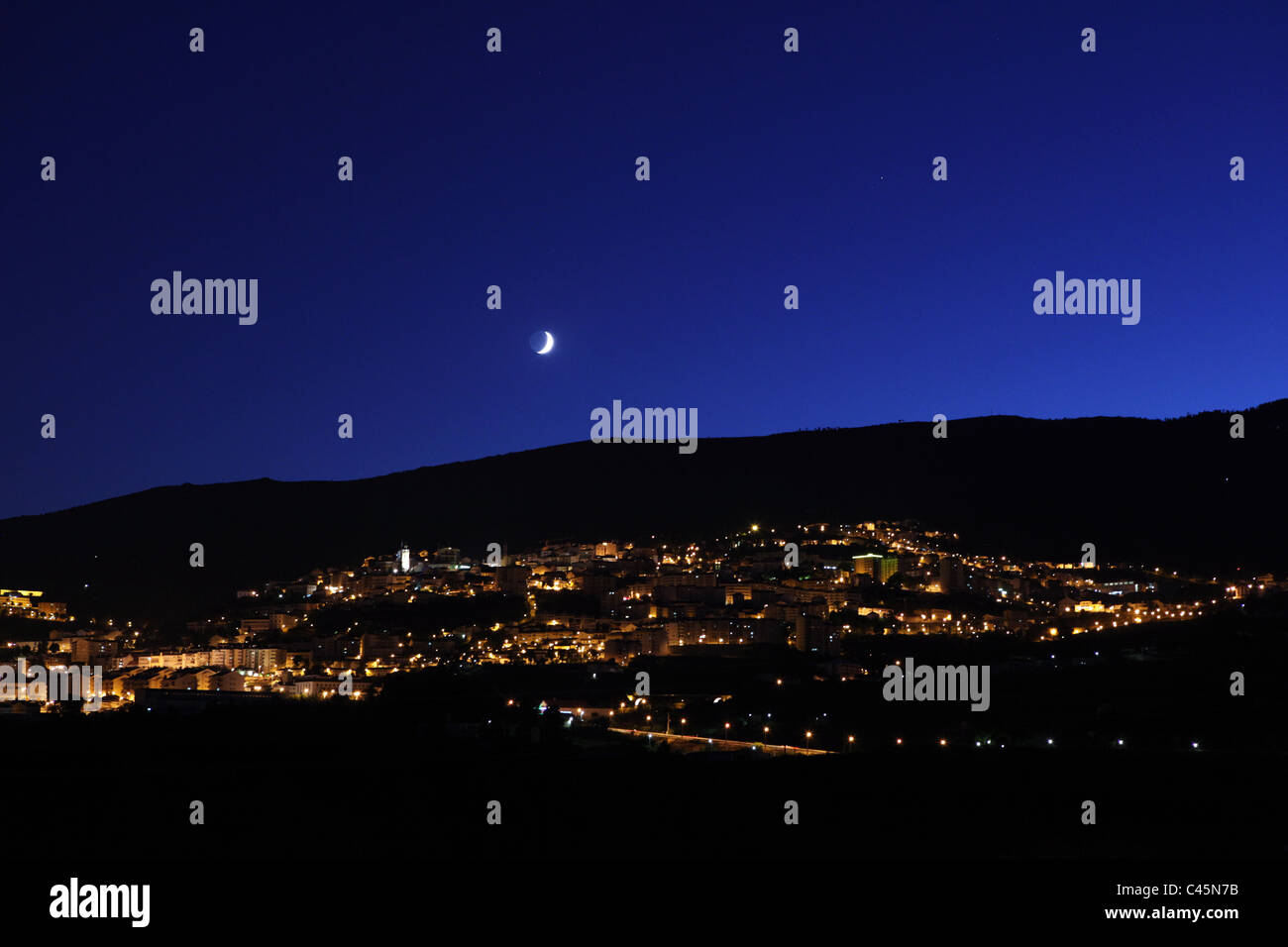 Le luci della città di Covilhã, in Portogallo, al crepuscolo sotto una luna crescente Foto Stock