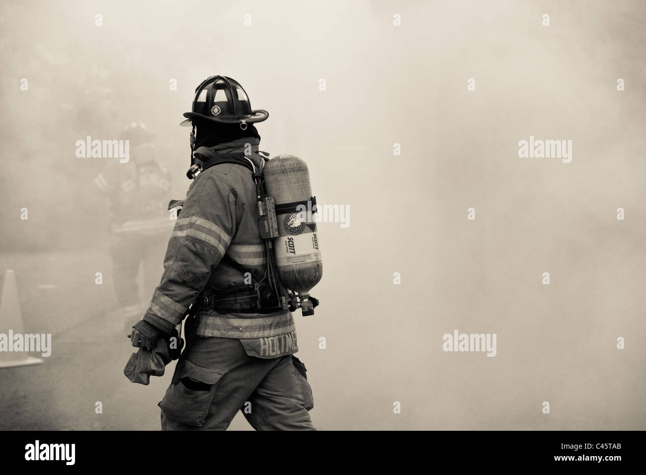 Vigile del fuoco nel fumo della casa di fuoco in pieno le attrezzature di protezione. Un secondo vigile del fuoco è visibile attraverso il fumo Foto Stock